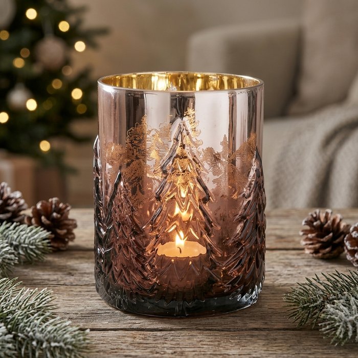 Tanny brown glass windlight glowing with a lit tealight on a rustic wooden table surrounded by pine cones and frosted fir branches with a Christmas tree in the background