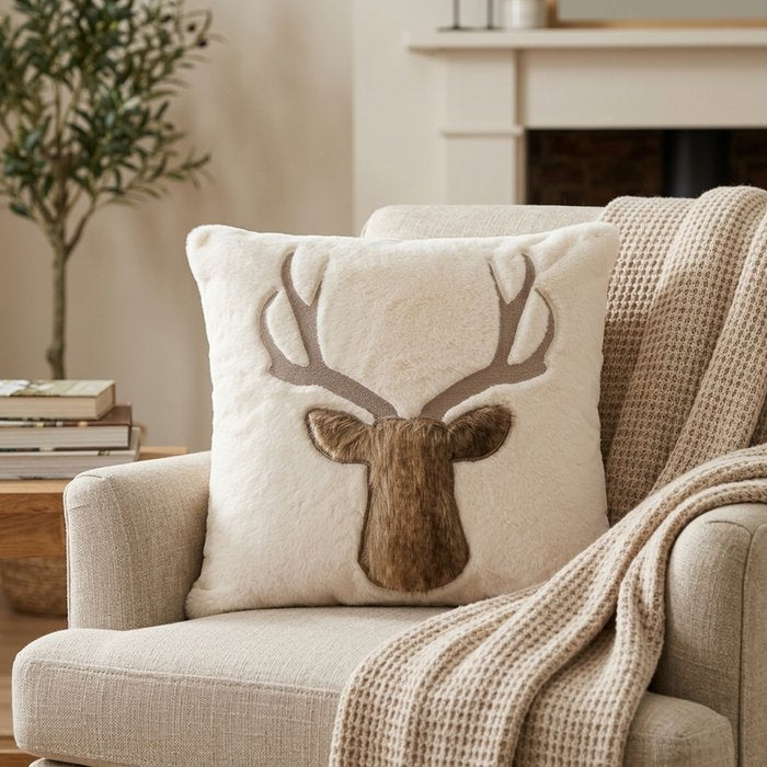 Cream Fenro cushion with a brown embroidered deer motif styled on a neutral armchair with a knitted throw