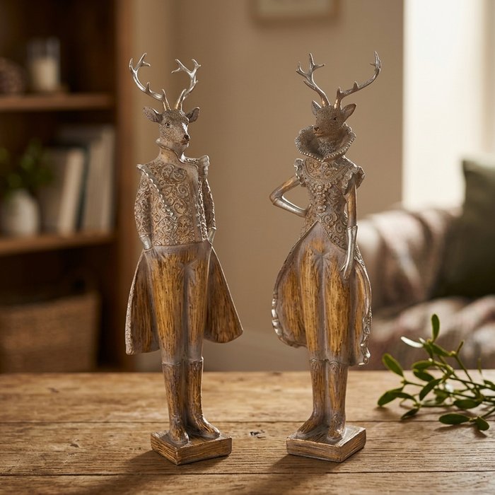 Pair of dressed stag and doe polyresin figurines in baroque-inspired outfits on a rustic wooden table with mistletoe in a warm Nordic interior