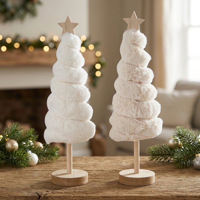 Two Elunara plush Christmas trees in cream white and beige with wooden star toppers styled on a rustic table with pine branches and warm bokeh lights