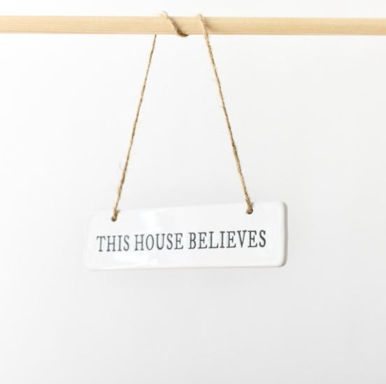 White ceramic This House Believes hanging sign with jute twine on a wooden rod
