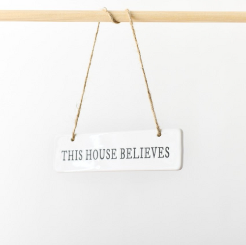 White ceramic This House Believes hanging sign with jute twine on a wooden rod