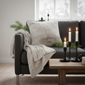 Moonstone faux fur cushion styled on a dark sofa with candlelight and pine branches in a cosy Nordic setting