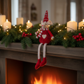 Red fabric sitting mouse with Nordic hat on a garland-dressed mantelpiece with candles and warm firelight glow