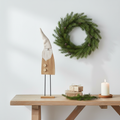 Tall wooden Santa gonk figurine on metal stand styled on a rustic console table with wrapped gifts, pine sprig and church candle in a Nordic entryway
